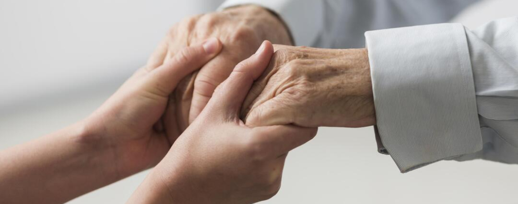 Manos de un cuidador brindando apoyo a las manos de un paciente de edad avanzada, ilustrando el acompañamiento en enfermedades neurodegenerativas como el Parkinson.