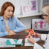 Una doctora ginecóloga utiliza un modelo anatómico del útero para explicar chequeos médicos preventivos a una paciente, representando el cuidado de la salud femenina en diferentes etapas de la vida.