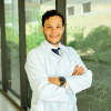 Retrato del Dr. Andrés Felipe Porto Mercado, médico del Hospital Serena del Mar, vistiendo bata blanca, camisa y corbata. El Dr. Porto, egresado de la Universidad del Rosario y especialista de la FUCS, posa sonriente con los brazos cruzados en un pasillo moderno y luminoso del hospital.